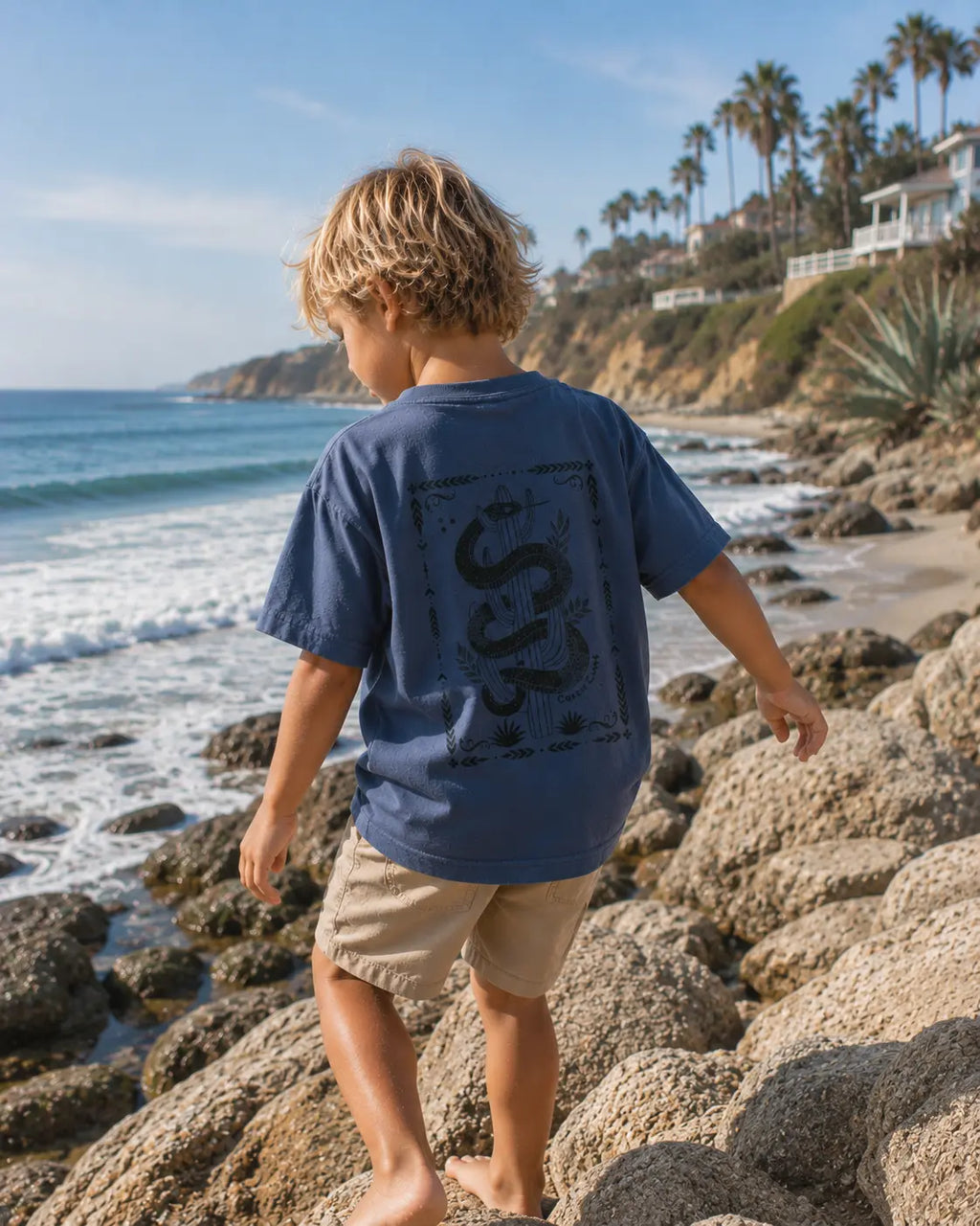 Back view of boy wearing Cooee Coast, coastal flow tee desert sea featuring back print sea serpent.