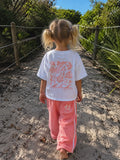 Back view of girl wearing Cooee Coast, coastal flow tee featuring peach back print
