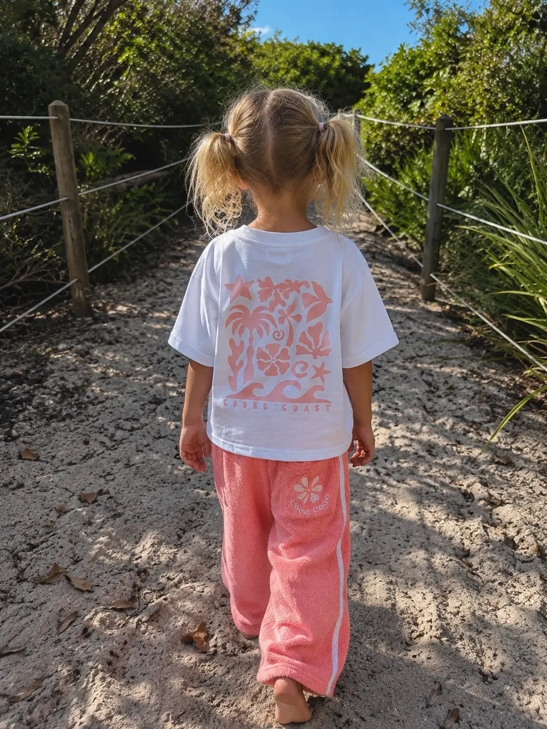 Back view of girl wearing Cooee Coast, coastal flow tee featuring peach back print