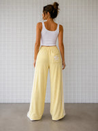 Backview of woman wearing Cooee Coast Lemon retro terry pants featuring embroidered back pocket, relaxed fit.