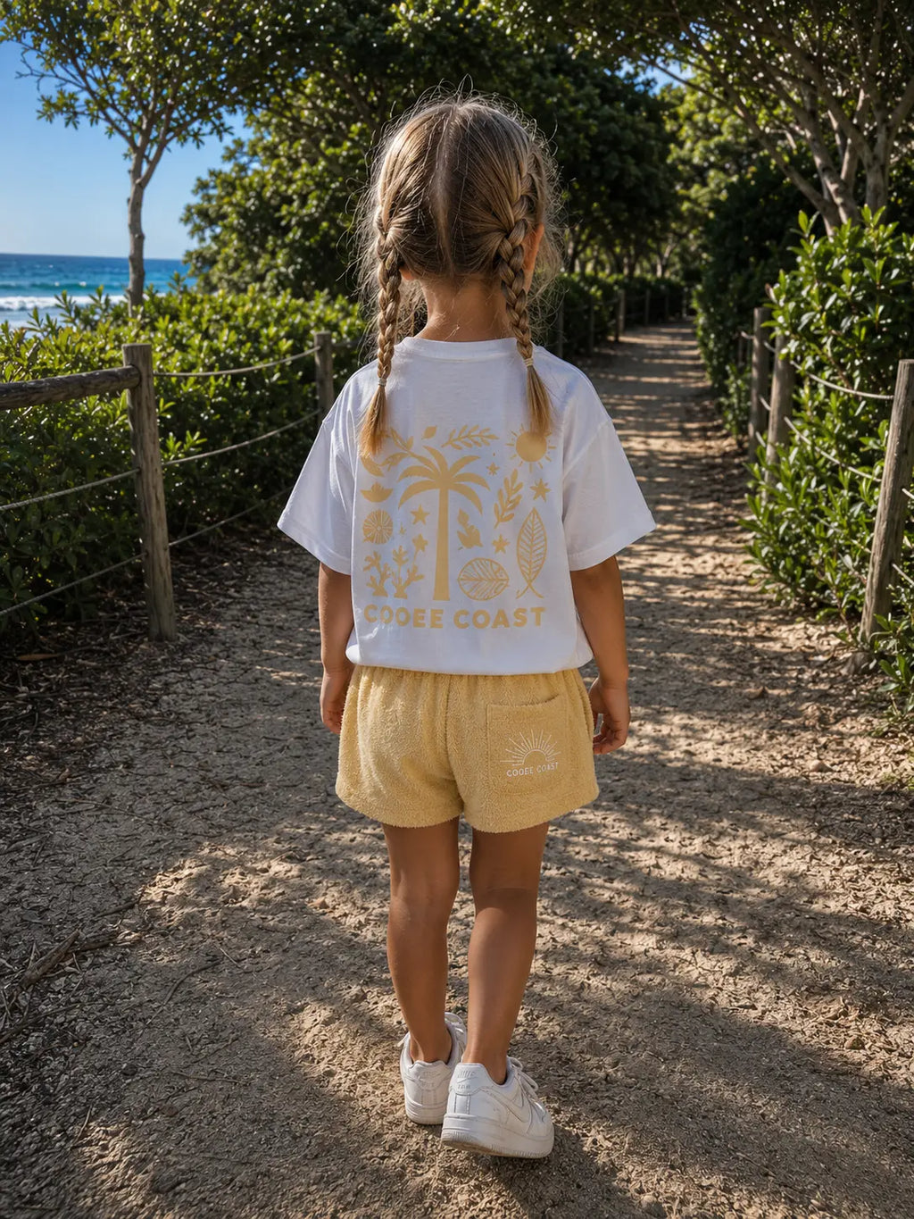 Back view of a girl wearing Cooee Coast Lemon Sorbet terry shorts featuring embroidered back pocket, relaxed fit.