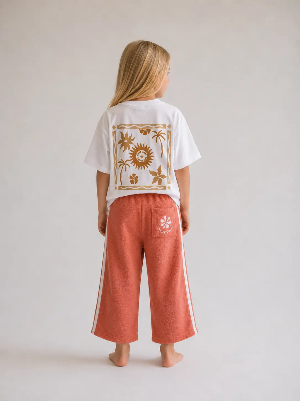 Back view of girl wearing Cooee Coast peach retro terry pants featuring embroidered back pocket, relaxed fit.