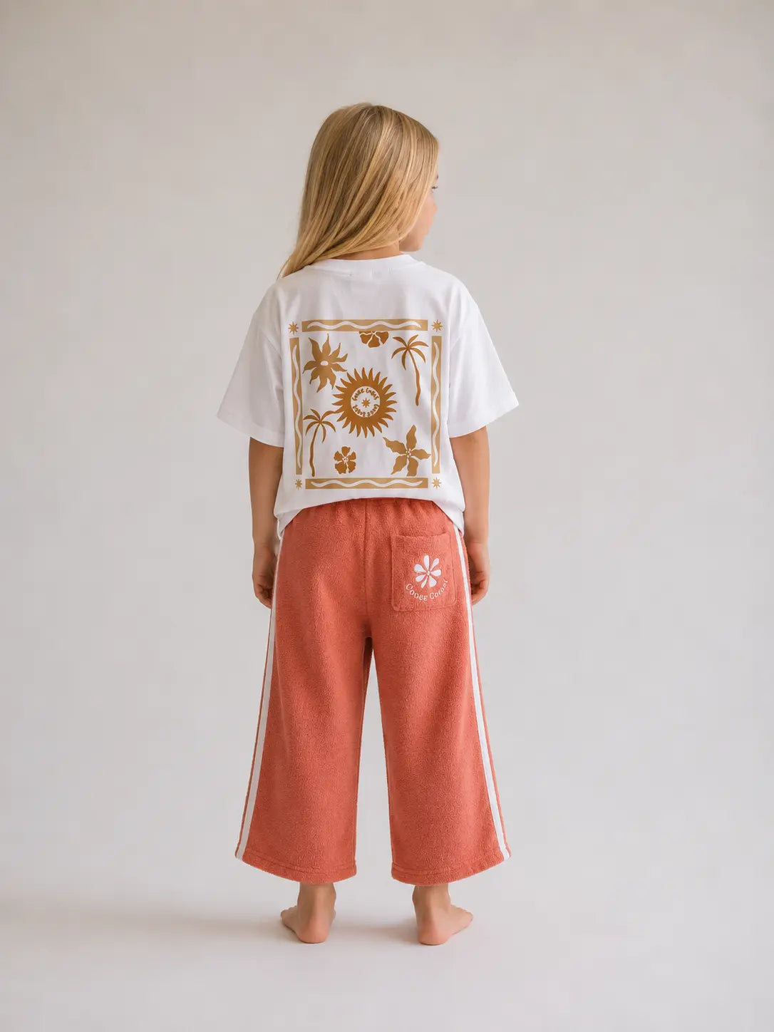 Back view of girl wearing Cooee Coast peach retro terry pants featuring embroidered back pocket, relaxed fit.