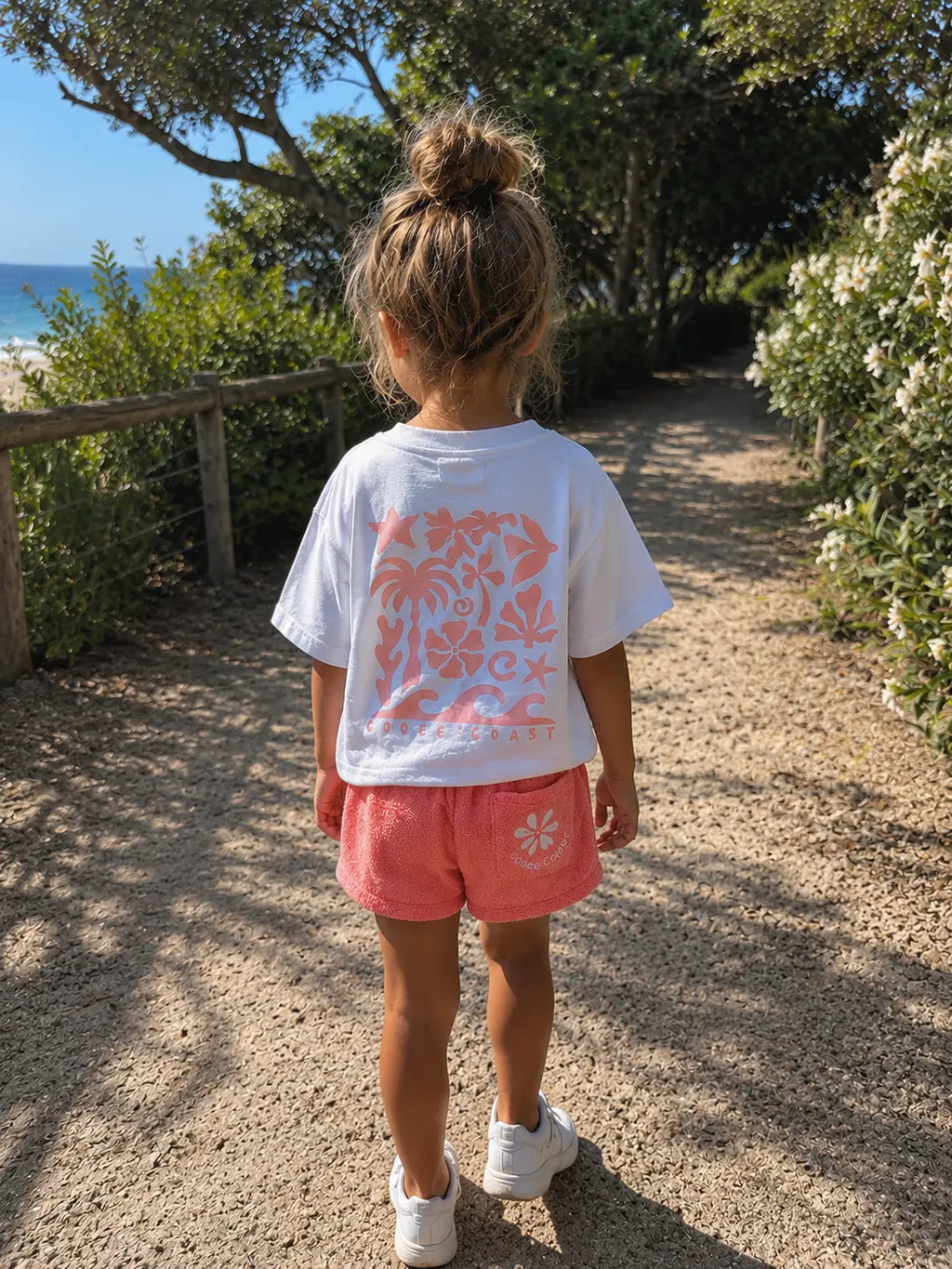 Back view of a girl wearing Cooee Coast Peach terry shorts featuring embroidered back pocket, relaxed fit.