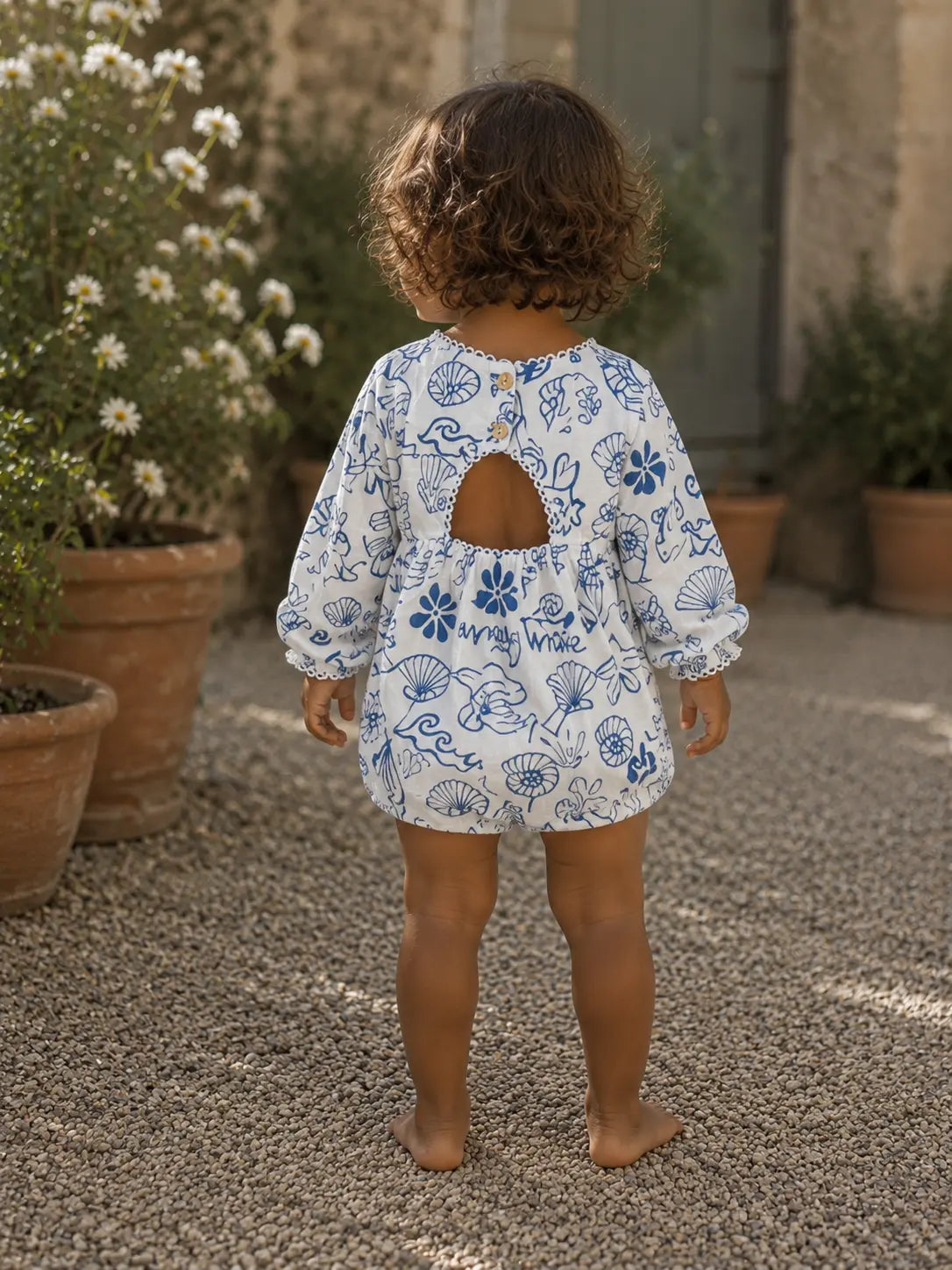 Back:
Back view of baby wearing Cooee Coast Amore Romper featuring open back and wooden button detail.