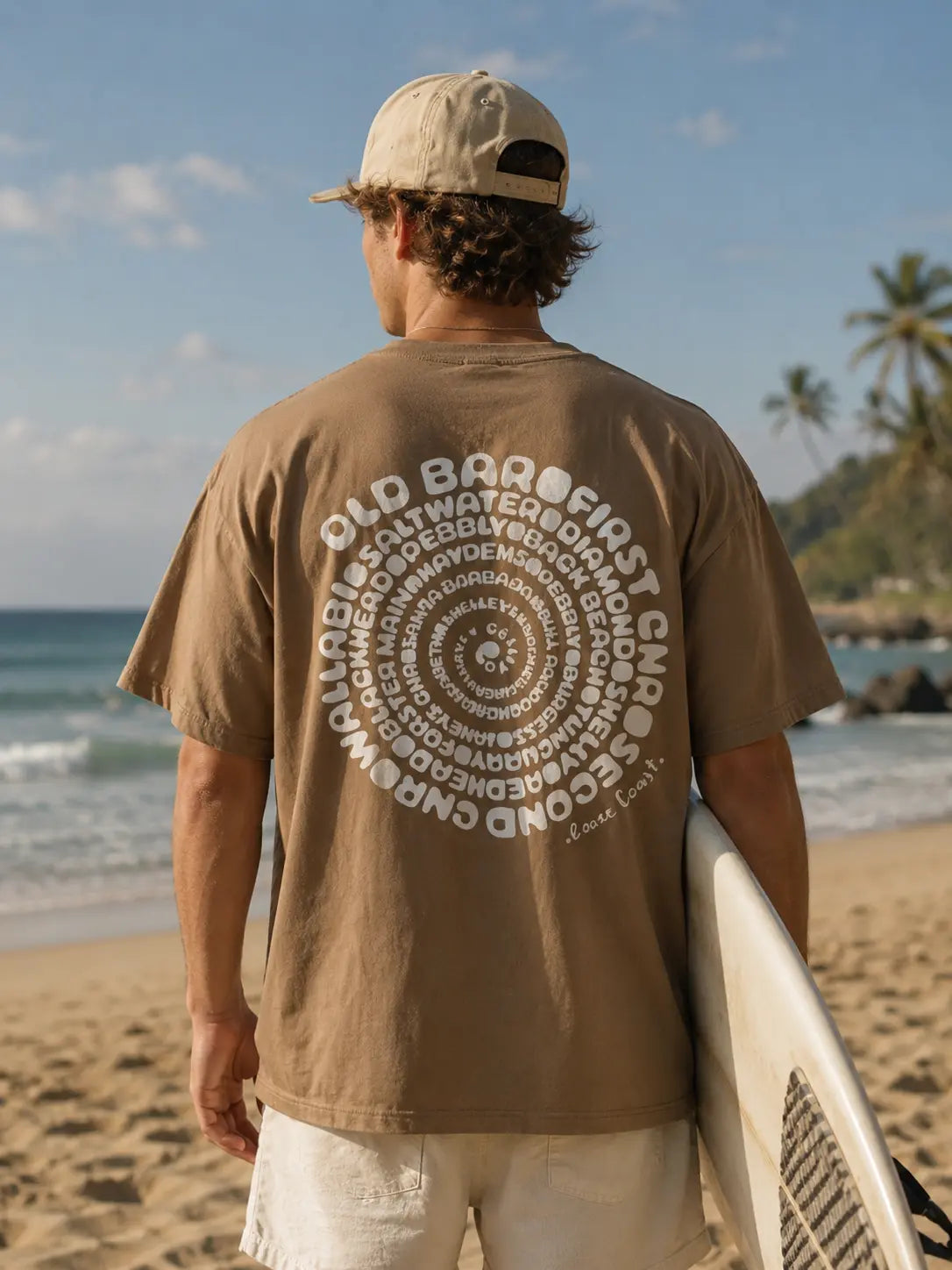 Man holding surfboard wearing Cooee Coast Men’s Tee in relaxed fit with soft premium cotton